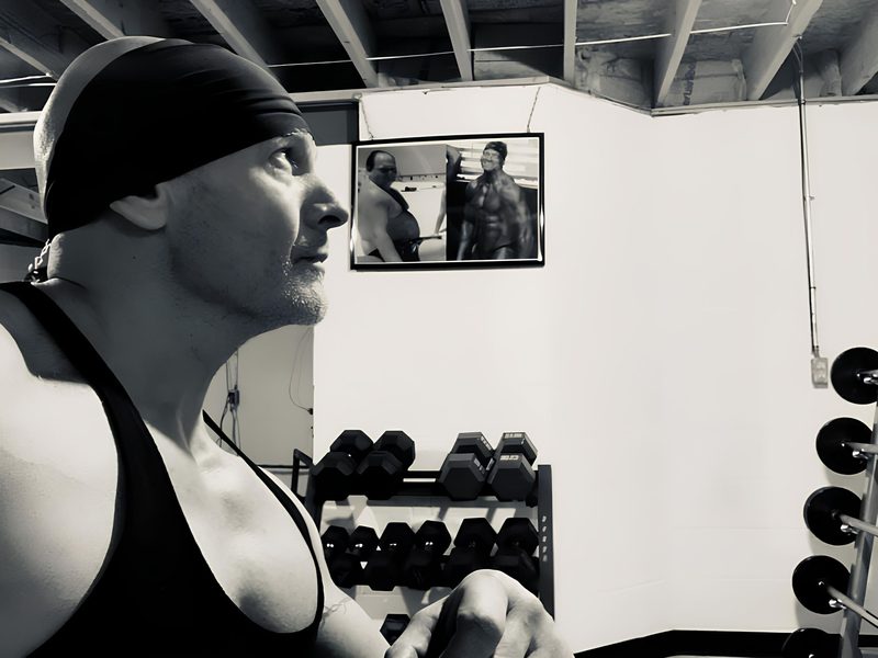 Philip Albenze in profile in a black tank top, in his gym