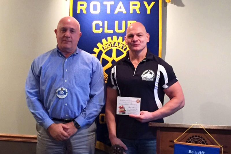 Phil holding a certificate beside a Rotary Club member in front of the Rotary banner