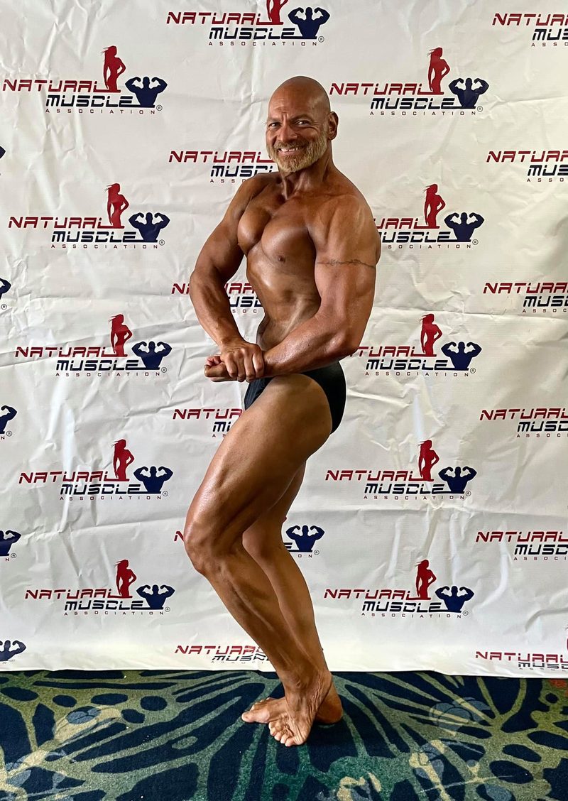 Phil hitting a side-chest pose in front of a Natural Muscle backdrop